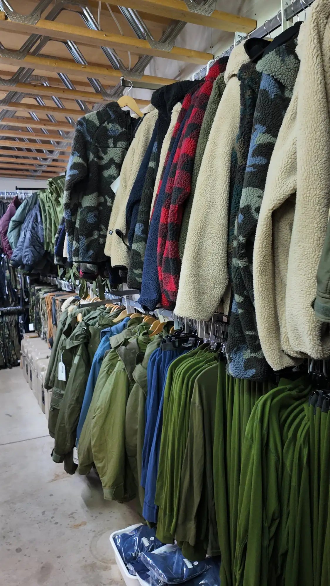 Une rangée de vestes douillettes doublées de polaire, dans divers motifs de camouflage et de carreaux, est suspendue proprement à des cintres en bois.
